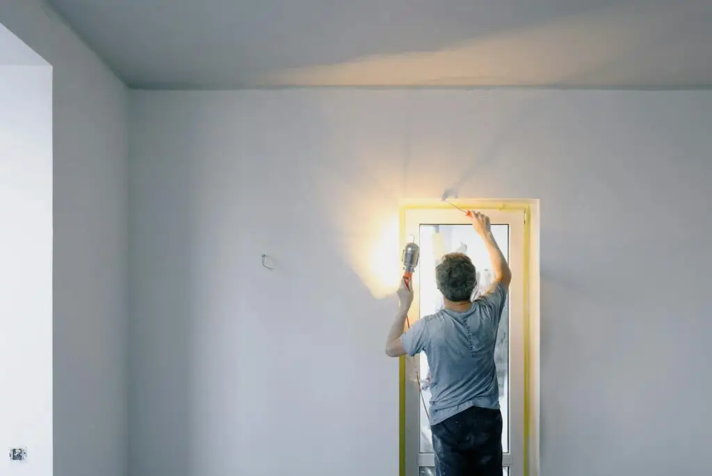 A handyman works on a home renovation project, painting a door indoors.